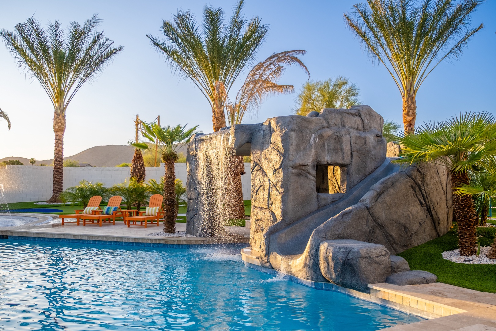 You'll love the resort-style pool with its dramatic rock waterfall and slide, framed by swaying palms and sunny poolside loungers under open desert skies.