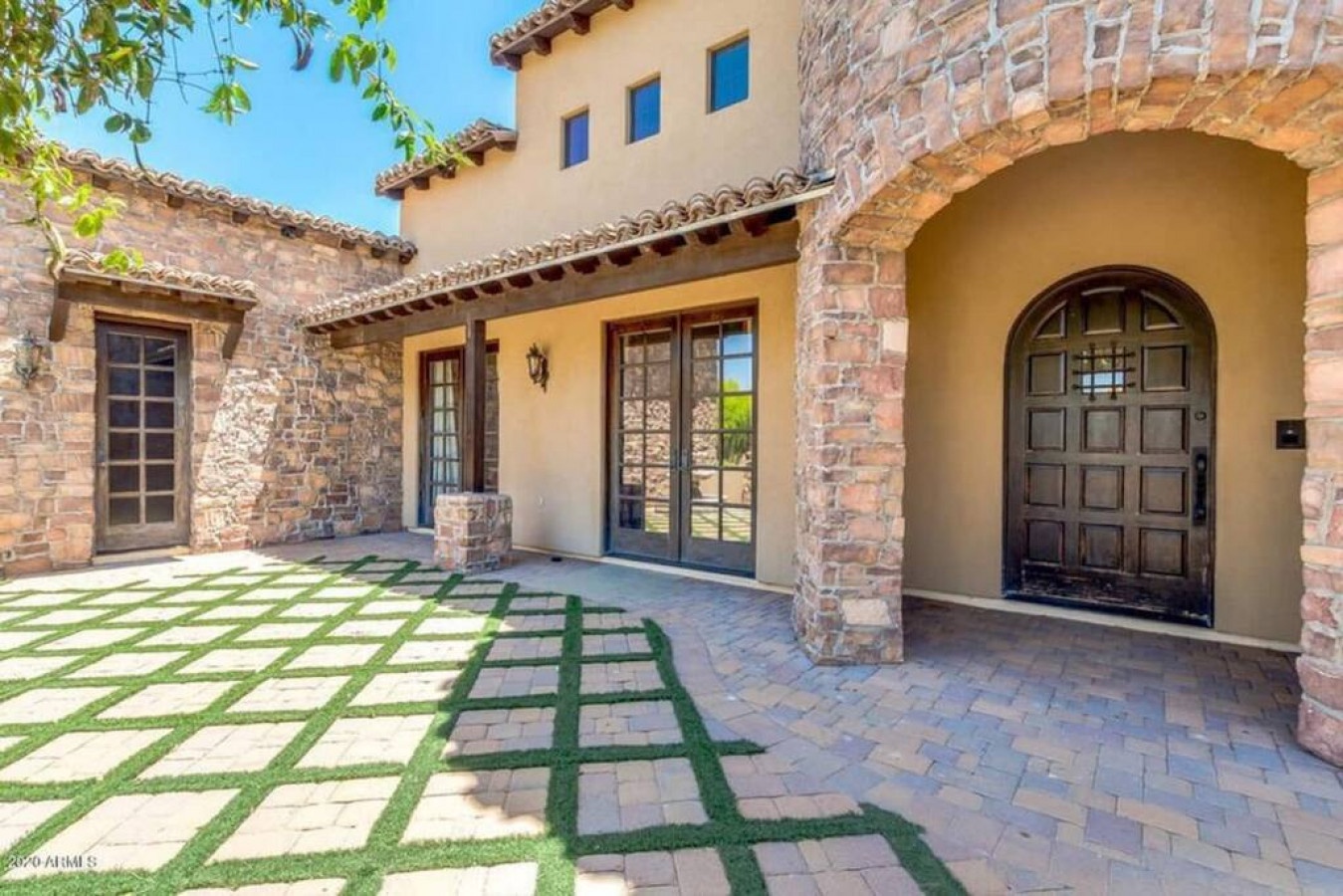 Mediterranean villa entrance with rustic stone archway, warm stucco walls, and charming tile roof details.