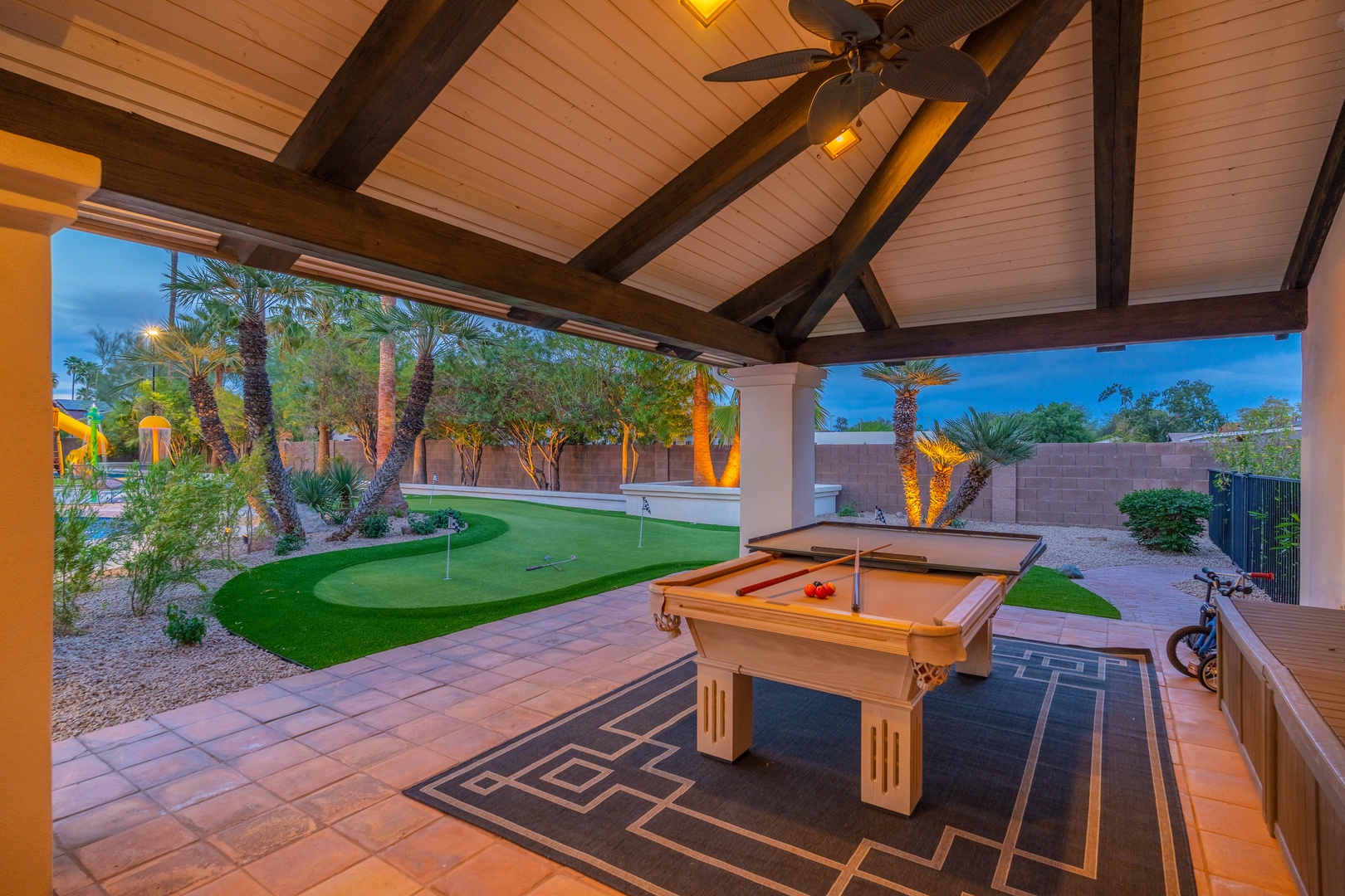 Your private covered patio opens to a putting green and desert-landscaped backyard, complete with a pool table for evening entertainment under elegant wood-beam ceilings.