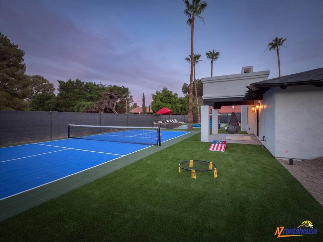 Modern vacation home with private tennis court, outdoor games, and tropical palm trees under twilight skies.
