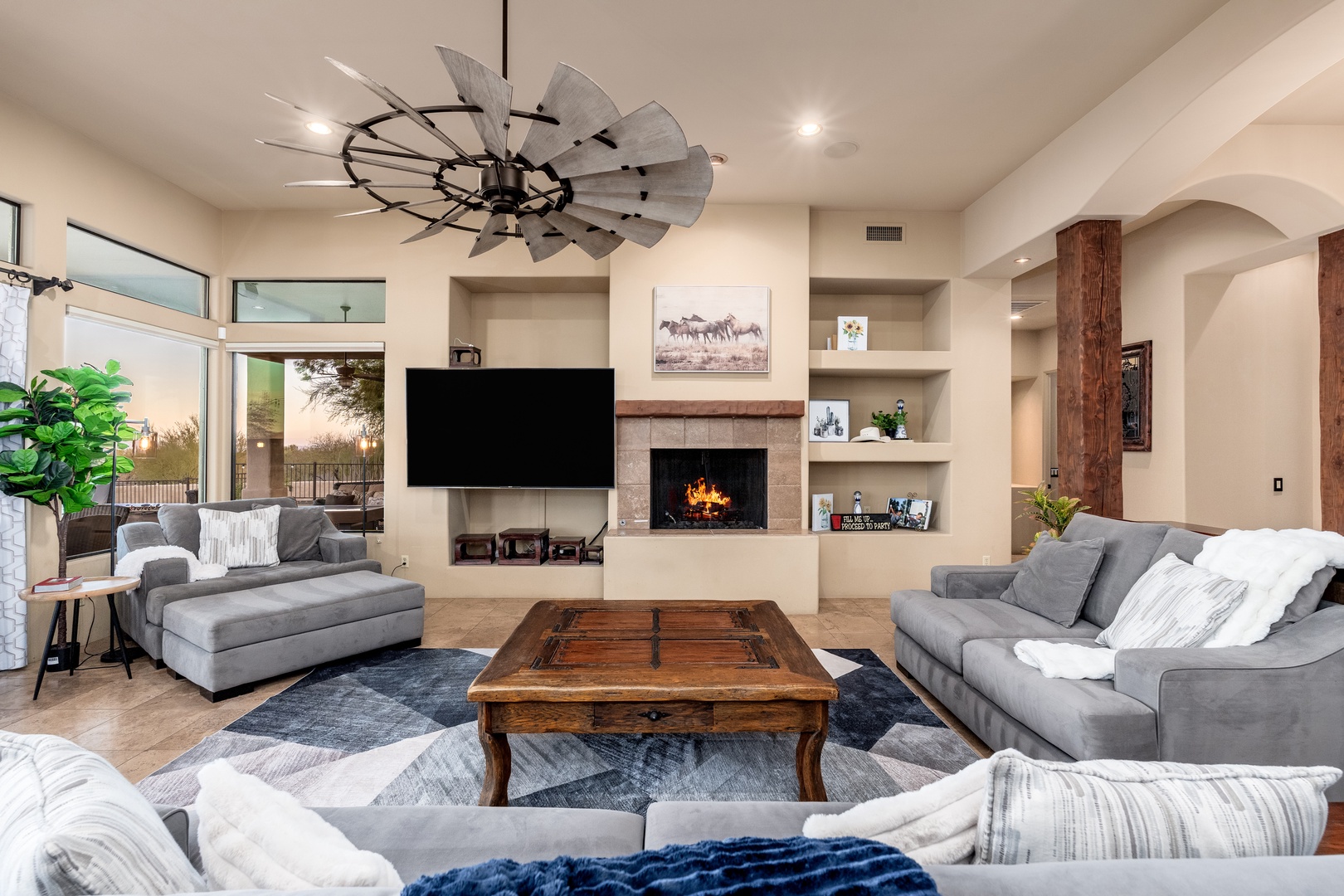 Sink into plush sofas by the fireplace, where rustic wood accents and a statement windmill fan create your perfect retreat for movie nights and relaxation.