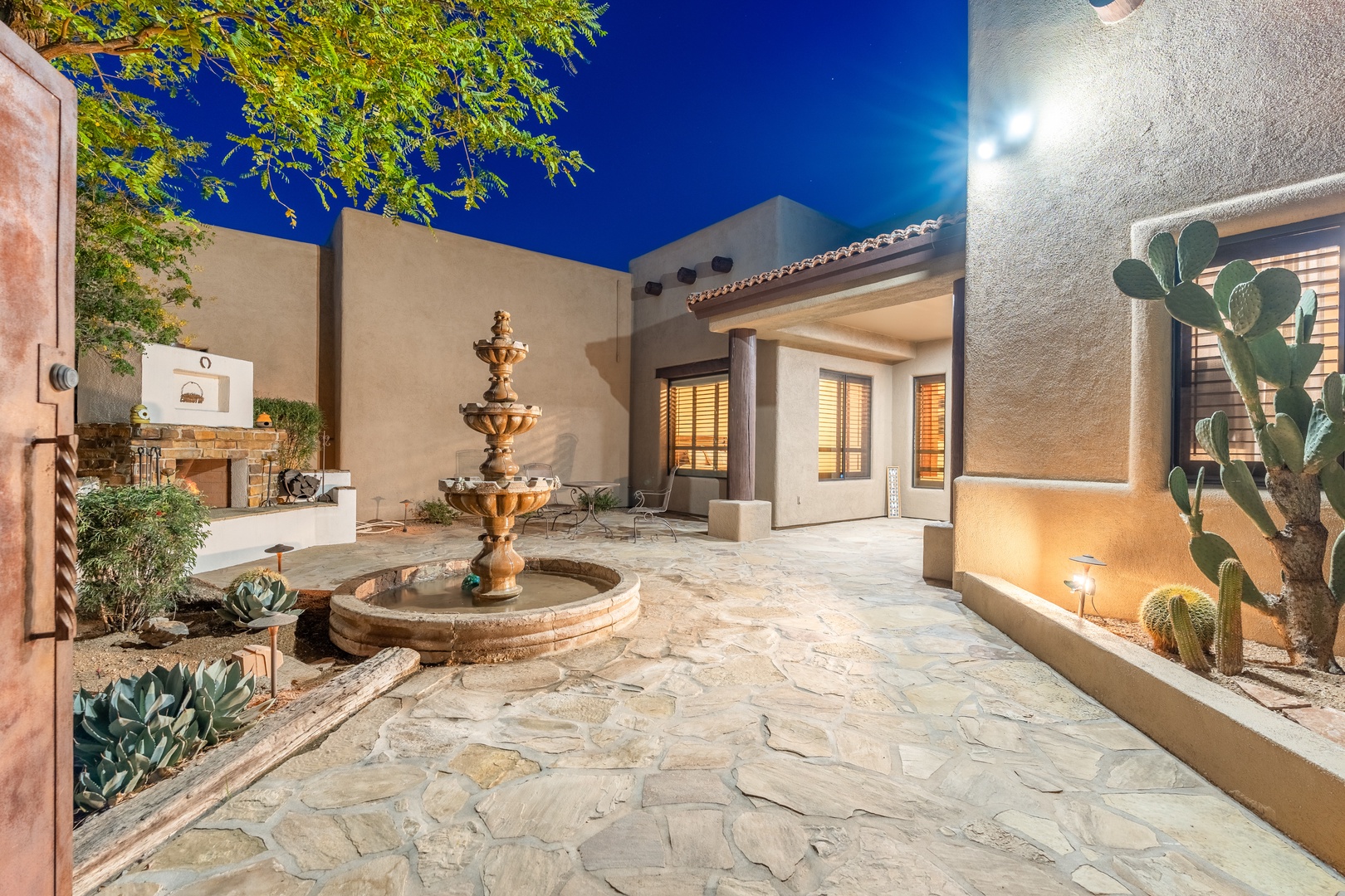 A tranquil inner courtyard featuring a tiered fountain, desert landscaping, and southwestern architecture under a brilliant twilight sky creates an inviting outdoor space for your stay.