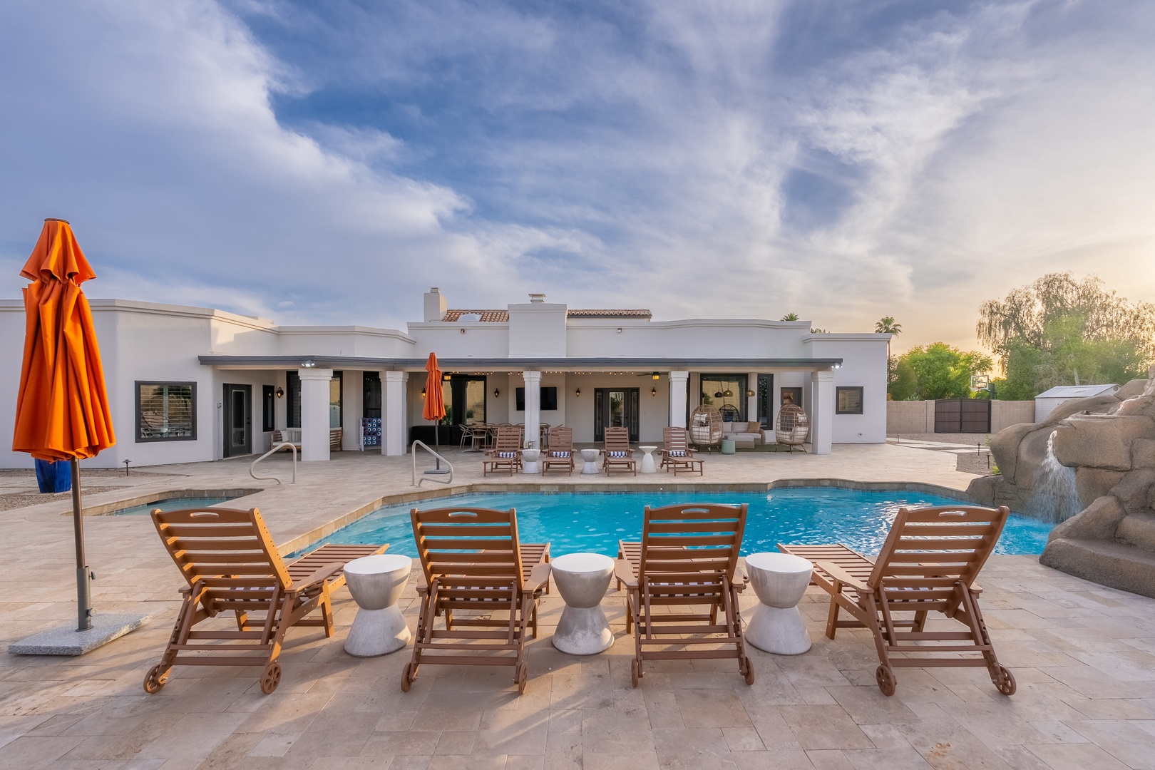 Expansive modern villa with pool, lounge seating, and covered patio featuring outdoor dining and scenic desert landscaping.