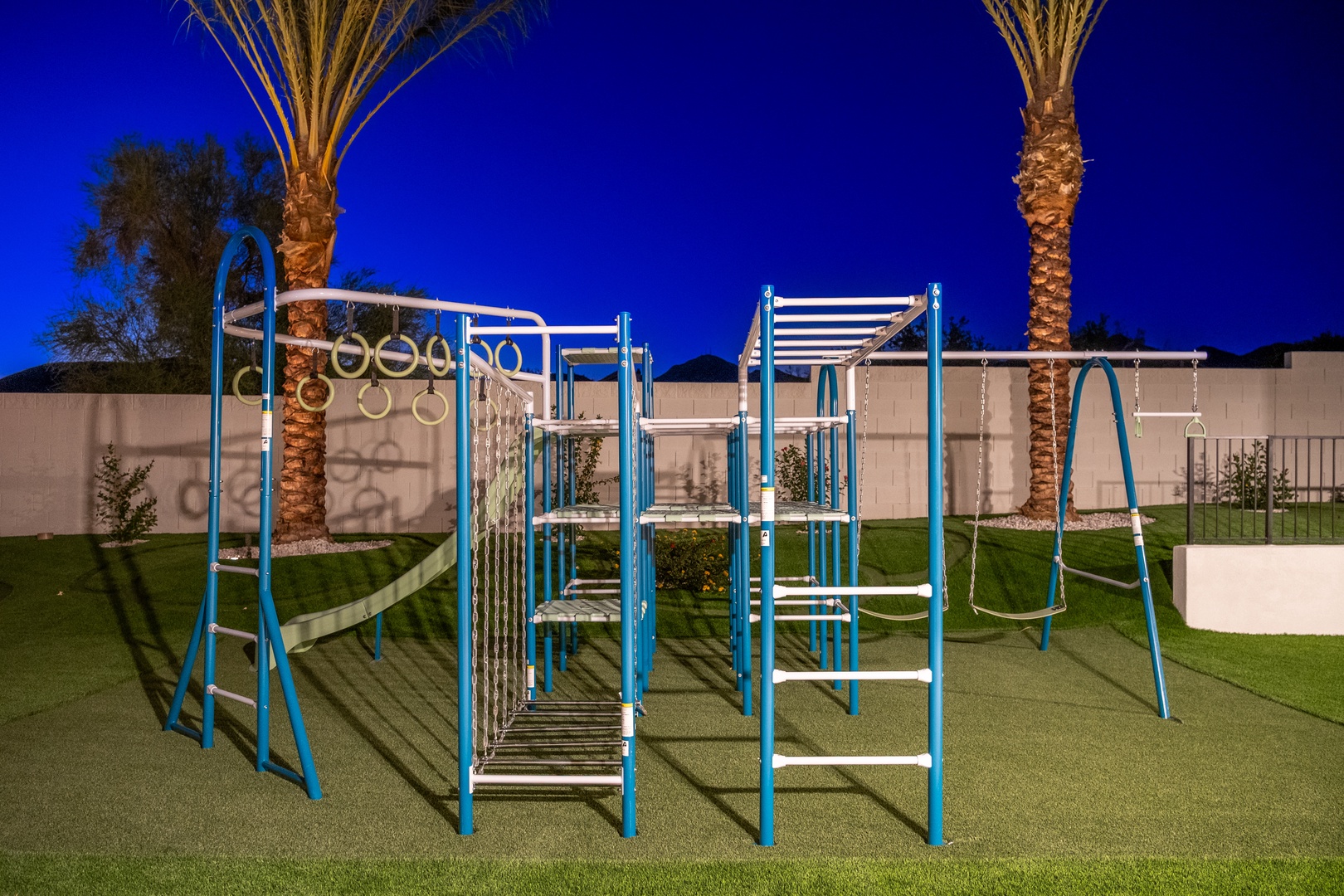 A fitness playground beneath the desert sky, featuring monkey bars, climbing elements, and swings—surrounded by palm trees and freshly manicured lawn for outdoor wellness activities.