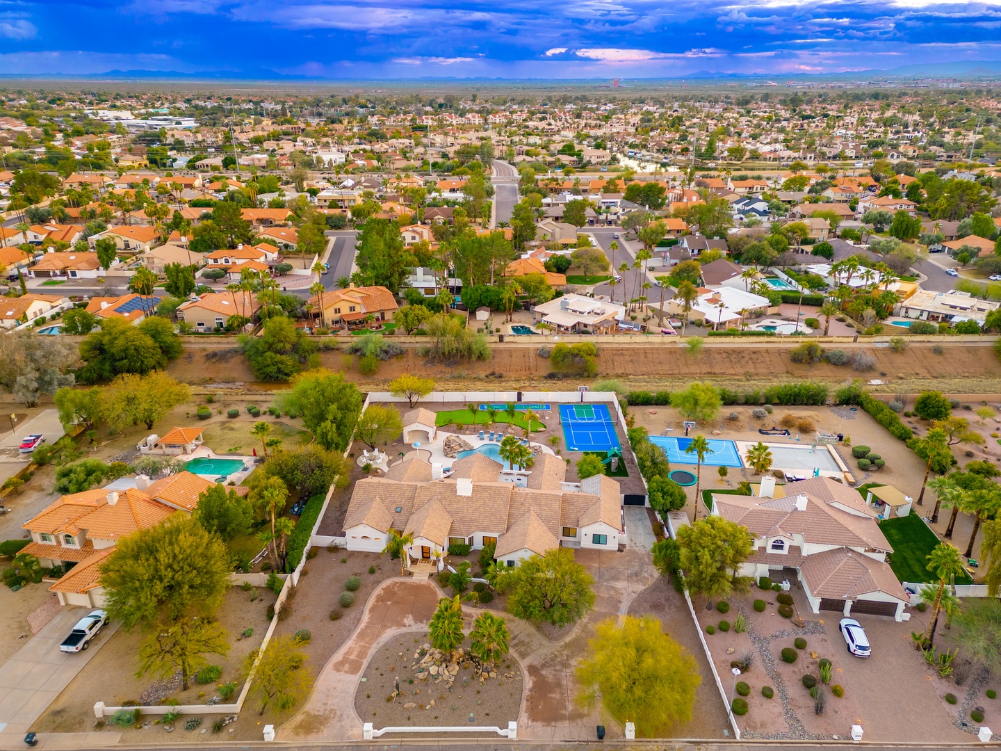 An aerial view showcasing the property's extensive grounds featuring multiple pools, sports courts, and spacious outdoor amenities set within a quiet residential neighborhood.