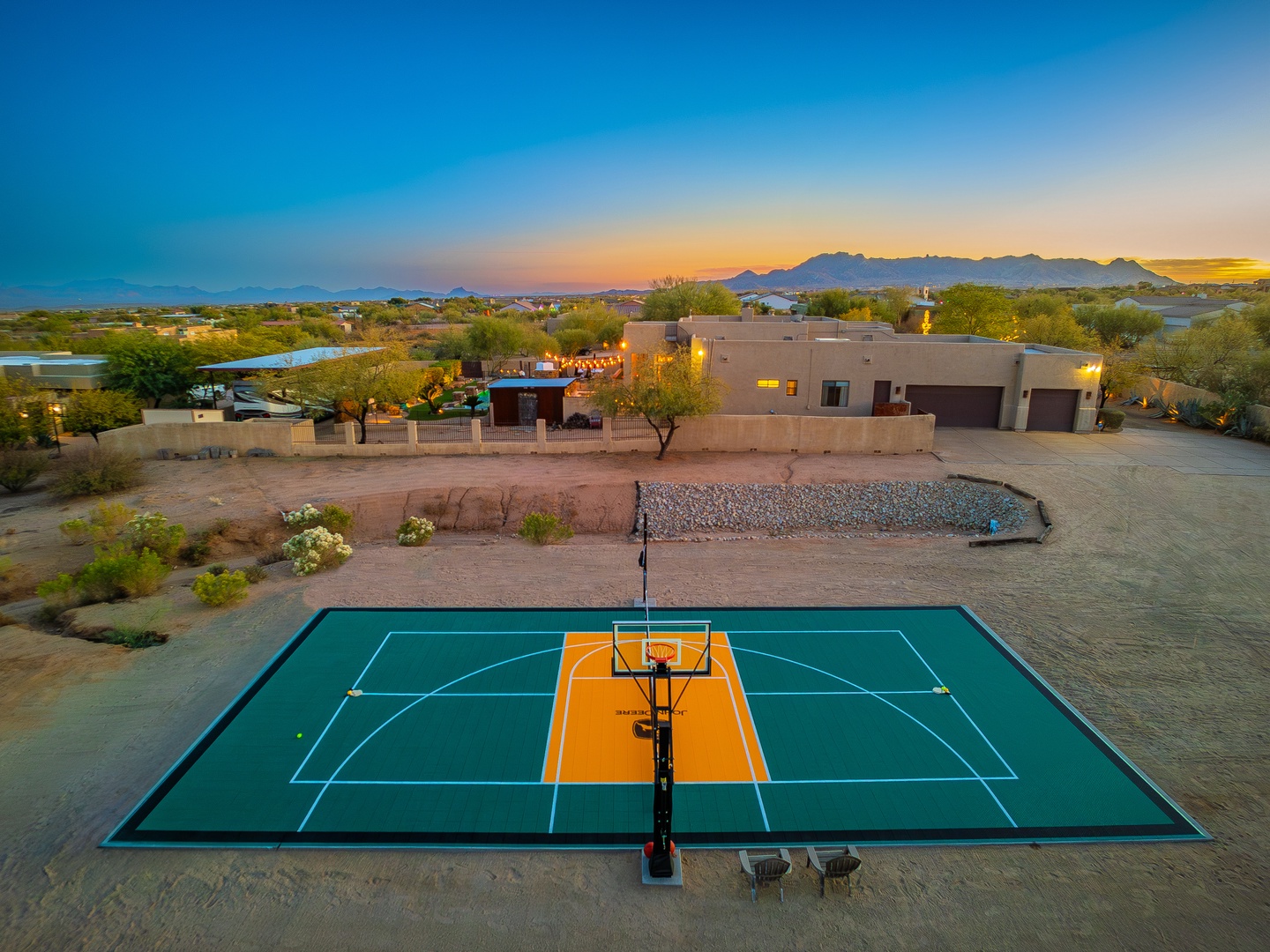 Aerial view of property featuring private basketball court surrounded by desert landscaping and mountain backdrop at sunset.