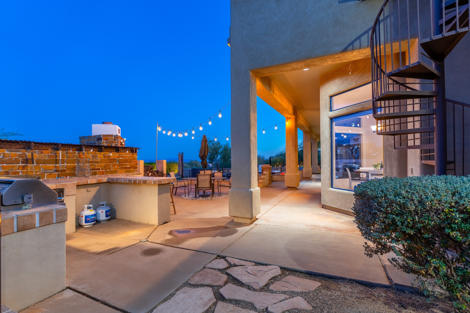 This inviting covered patio features a built-in BBQ area, outdoor dining space, and stylish lighting under the evening sky, perfect for memorable gatherings.