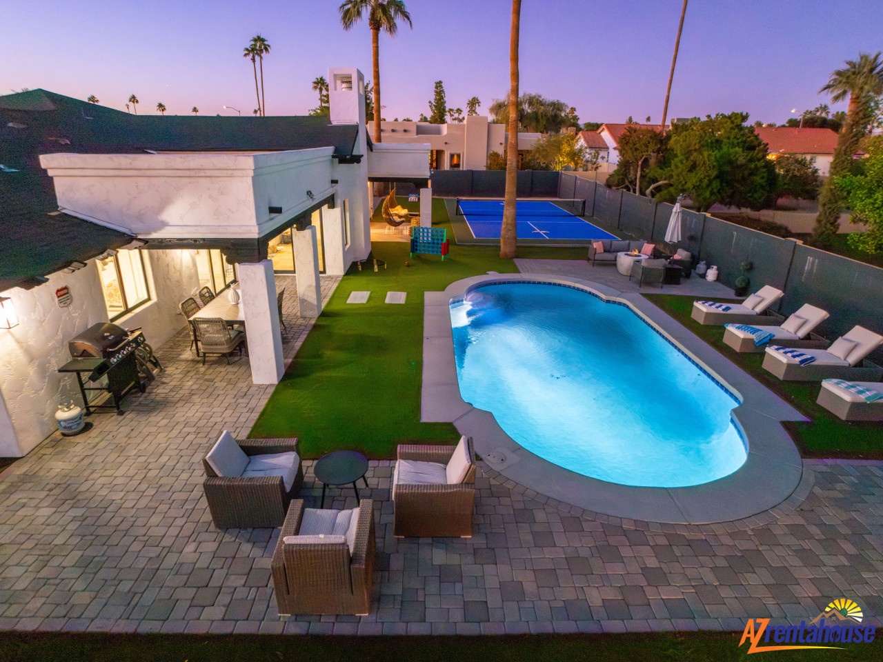 Aerial view of vacation rental property showcasing pool, sports court, and outdoor entertainment areas at twilight.
