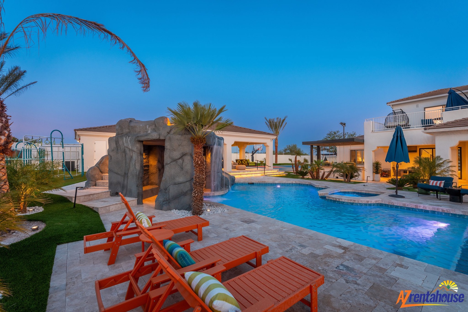 Stunning pool area with waterfall grotto, hot tub, and tropical landscaping creates your perfect desert oasis for evening relaxation.