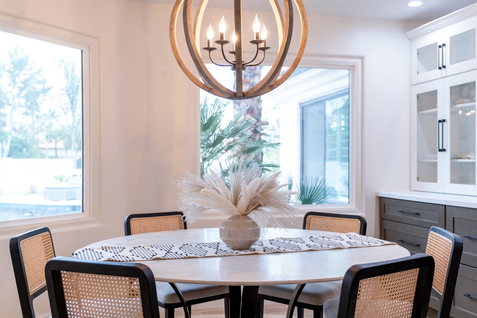 Gather around this inviting table where your mornings will be filled with natural light and warm conversations under an elegant chandelier.