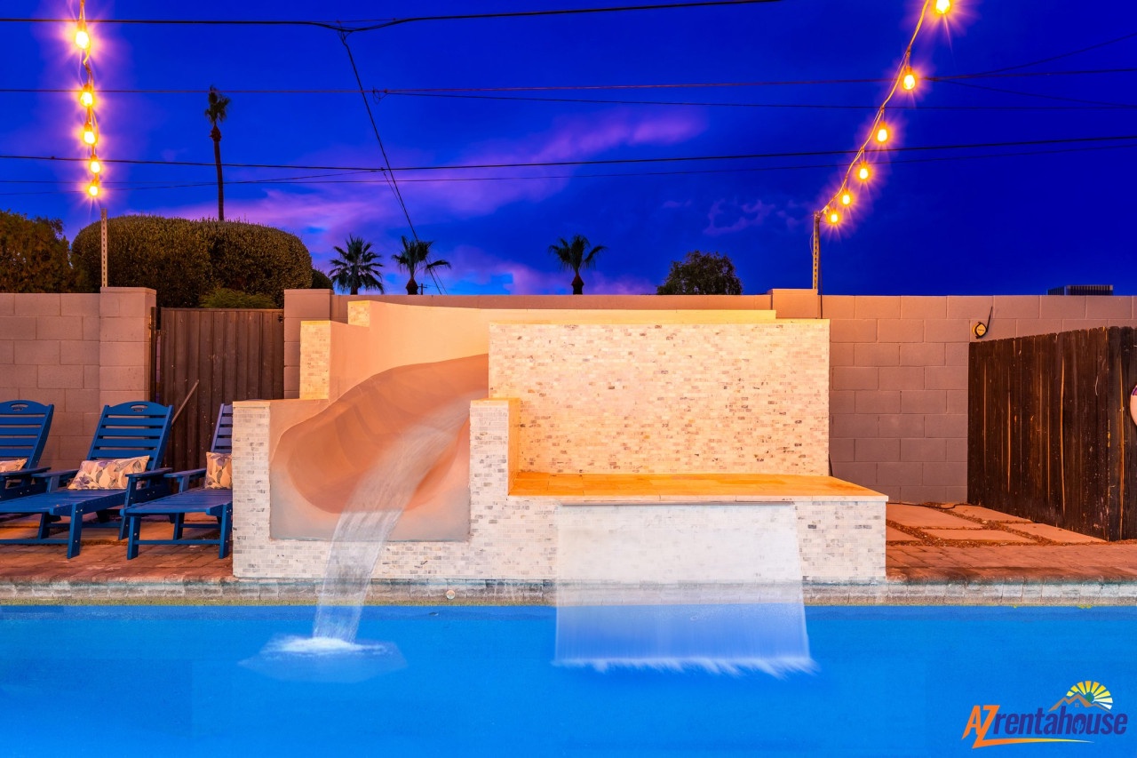 Dive into your private paradise with this stunning pool featuring a waterfall slide and hot tub, all illuminated by magical string lights.