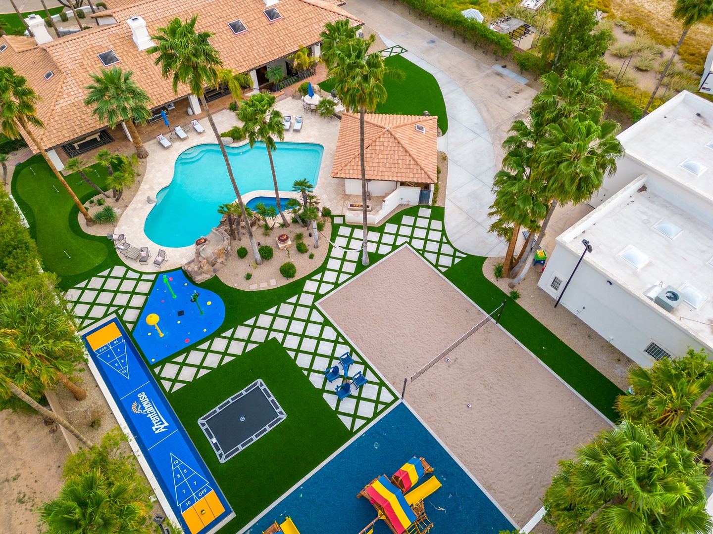 An aerial view captures the resort's expansive grounds, featuring a sparkling pool surrounded by palms, colorful playground equipment, and landscaped outdoor spaces perfect for families.