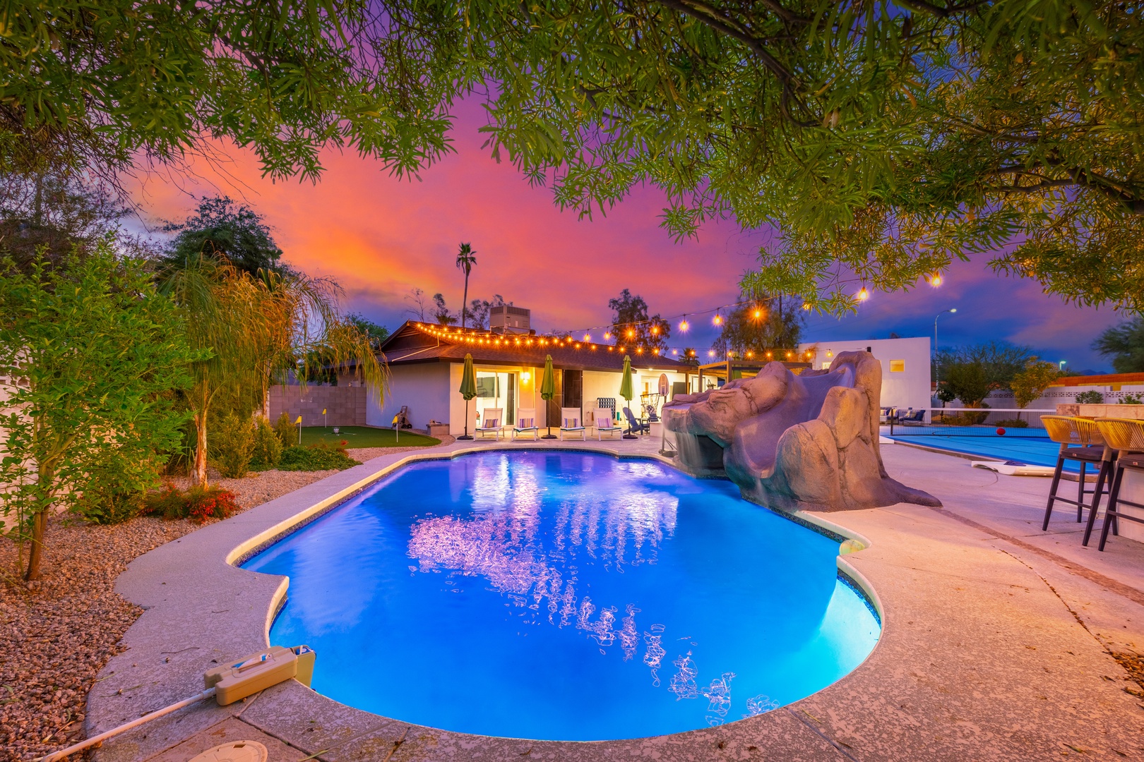Stunning backyard oasis with illuminated pool framed by desert palms and a vibrant twilight sky, perfect for memorable evenings under the stars.