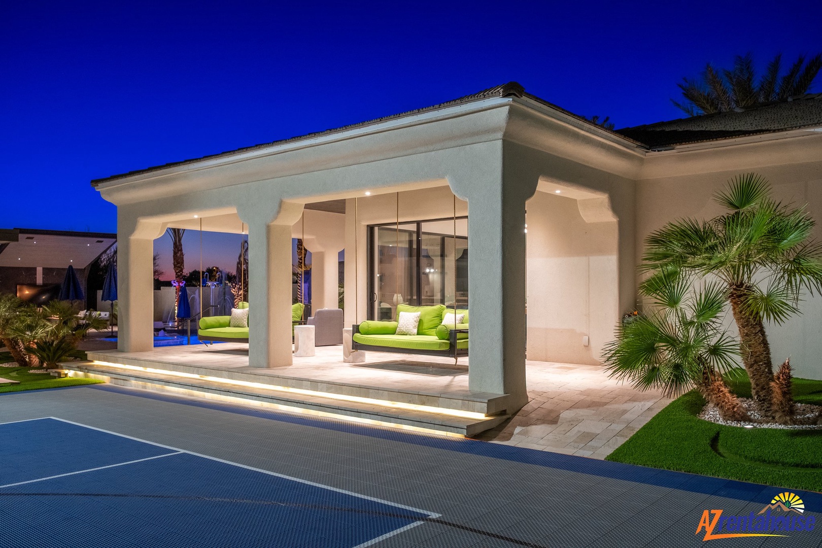Elegant white villa with covered outdoor lounge featuring bright green cushions, surrounded by palm trees and manicured gardens.