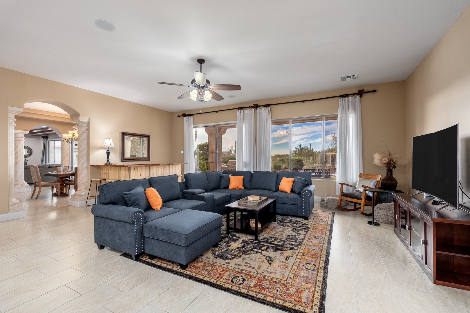 Relax in your spacious living room with comfortable sectional seating, a ceiling fan, and large windows framing stunning desert vistas—perfect for unwinding after your adventures.