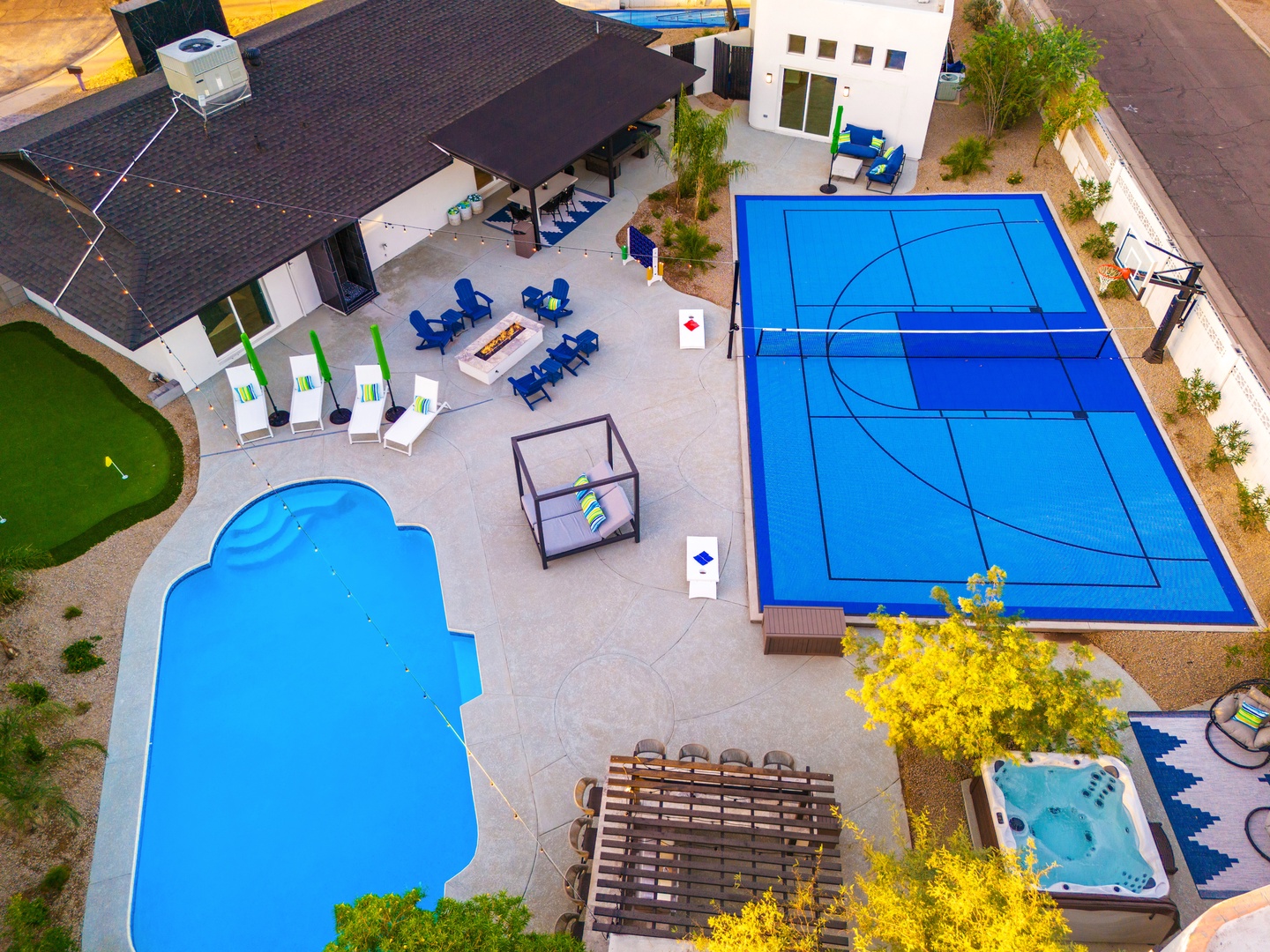Aerial view of a contemporary vacation property showcasing a heated pool, sport court, hot tub, putting green, and multiple outdoor entertainment zones perfect for group getaways.
