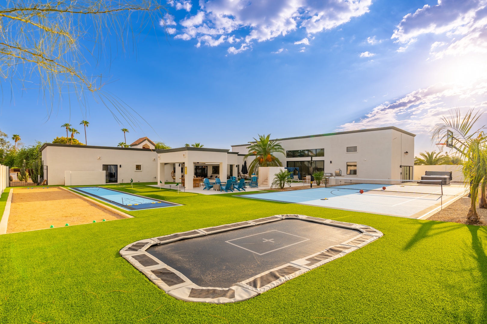 Modern desert retreat with sparkling pool, in-ground trampoline, and luxury outdoor living spaces beneath swaying palms and endless blue skies.