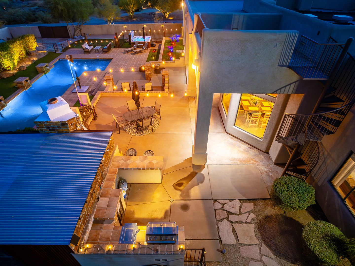 An aerial view at twilight reveals the property's stunning outdoor entertainment areas, including illuminated swimming pools, multiple lounging zones, and beautifully lit landscaping that creates an inviting ambiance for an evening gathering.
