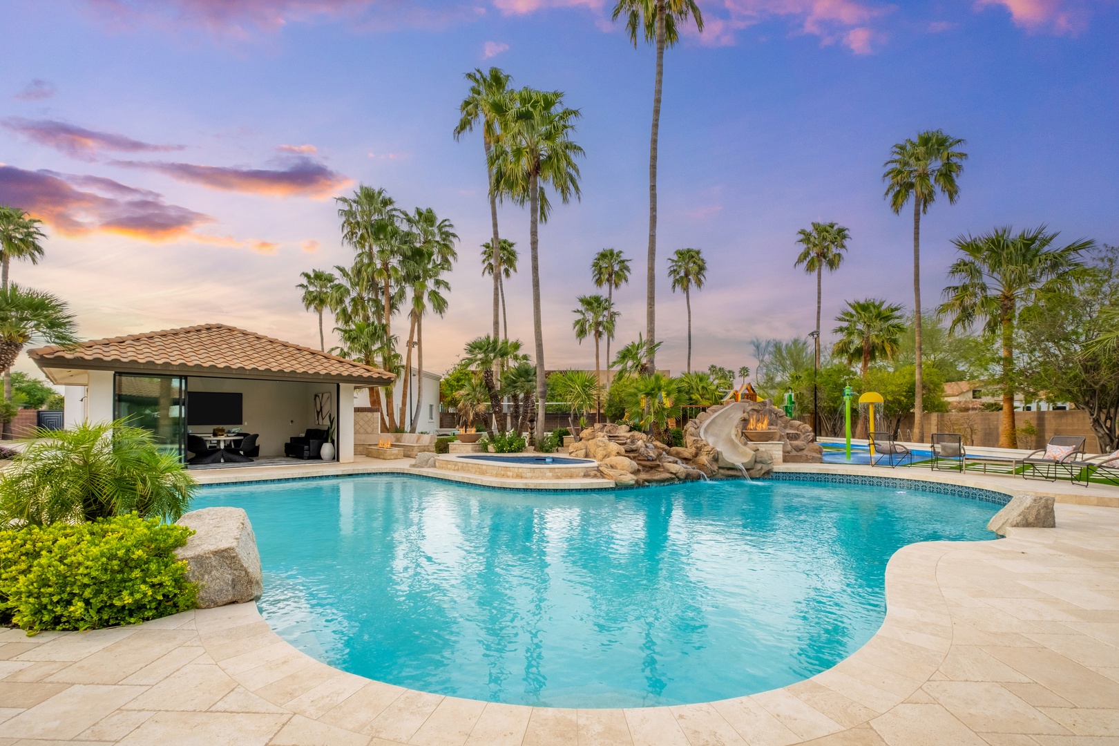 A stunning resort-style pool surrounded by swaying palm trees, perfect for basking under painted desert skies as the sun sets in brilliant hues of pink and gold.