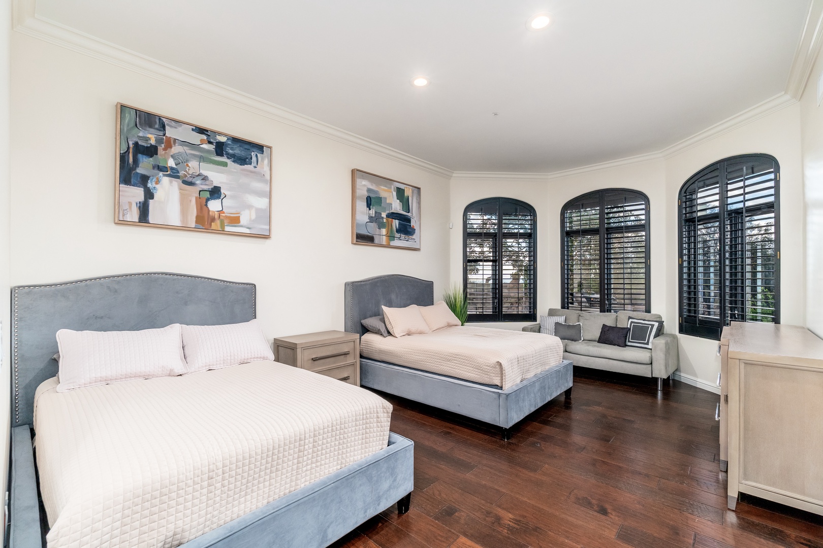 Sleep soundly in your elegant guest bedroom, featuring two plush beds with premium linens, rich hardwood floors, and arched windows with plantation shutters that frame natural light beautifully.