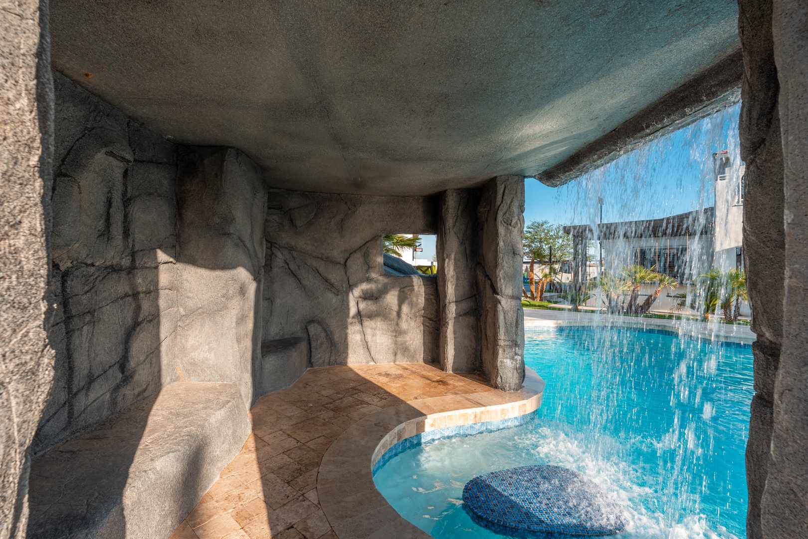 Themed cavern pool area featuring a waterfall feature, rocky grotto details, and resort-style aquatic facilities surrounded by tropical palms.