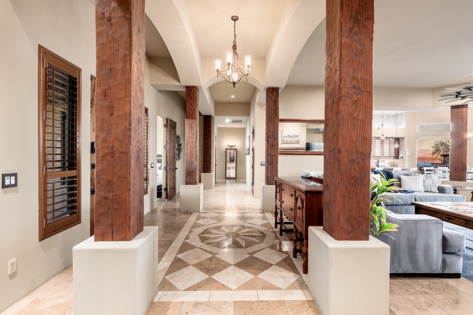 A striking entryway featuring soaring ceilings, warm wooden beams, elegant stone flooring with a decorative medallion, and an inviting chandelier that sets a welcoming tone.