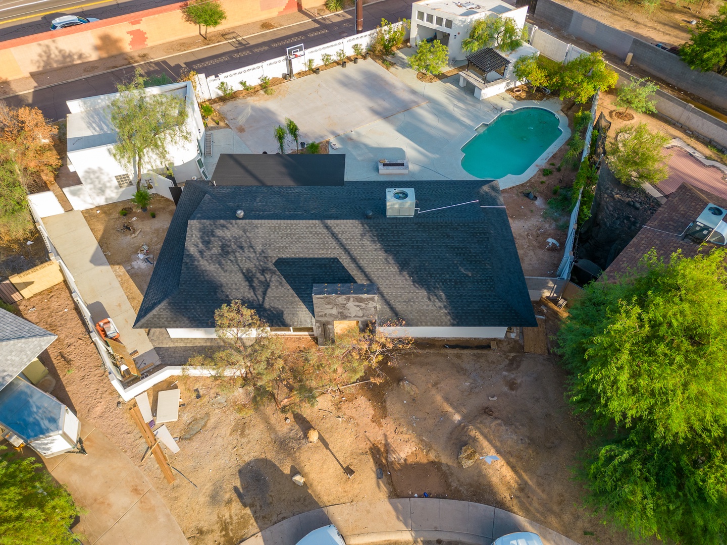Aerial view of the property showcasing the main building with a private pool, spacious outdoor areas, and surrounding neighborhood with mature trees and nearby street access.
