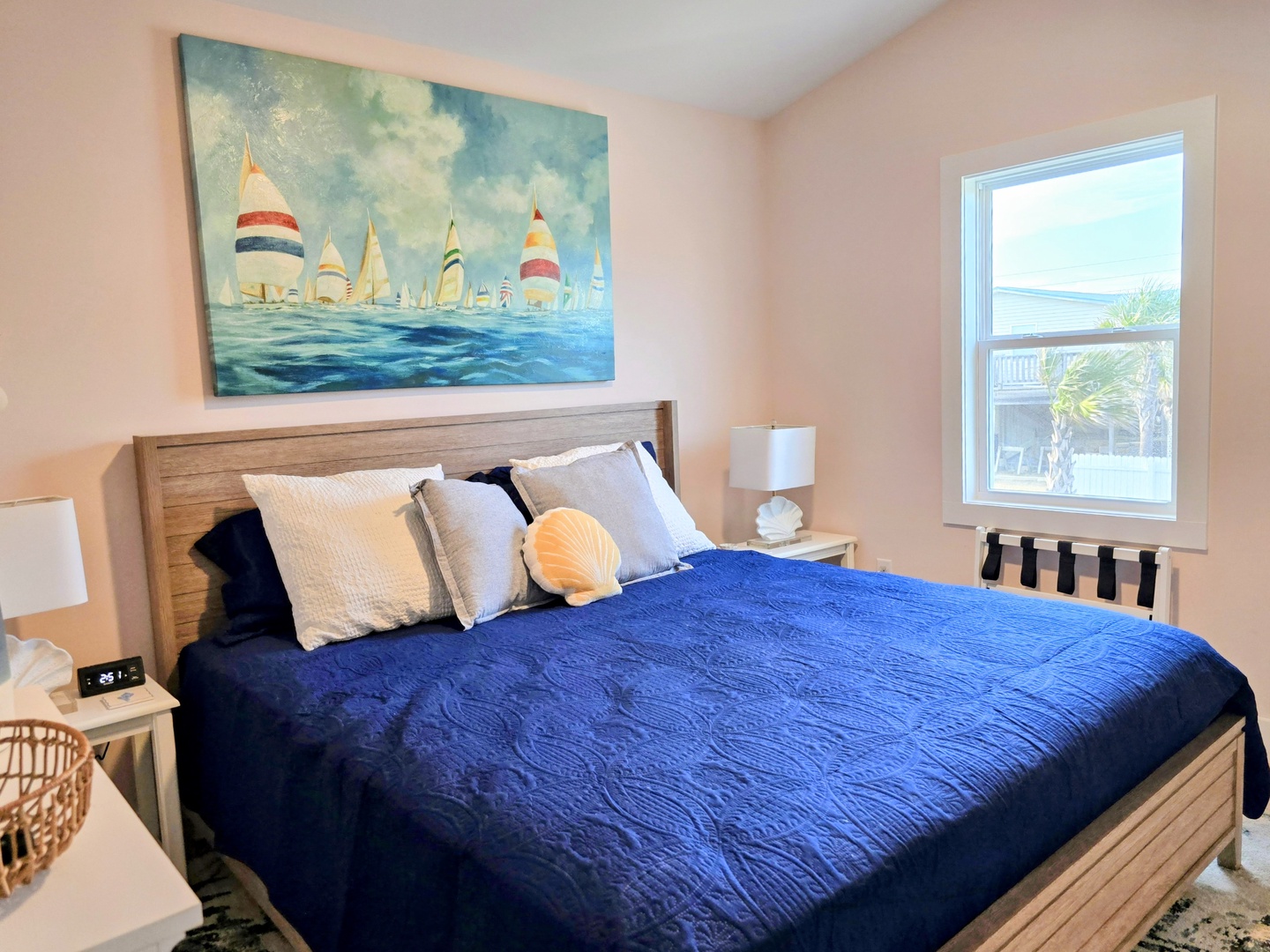 Drift off to sleep under coastal artwork in this serene bedroom featuring a plush blue comforter and peaceful sailboat painting.