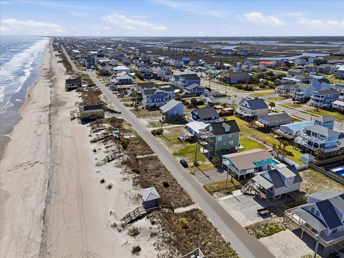 Aerial view of a coastal community with beach houses lining the sandy shore and ocean waves.