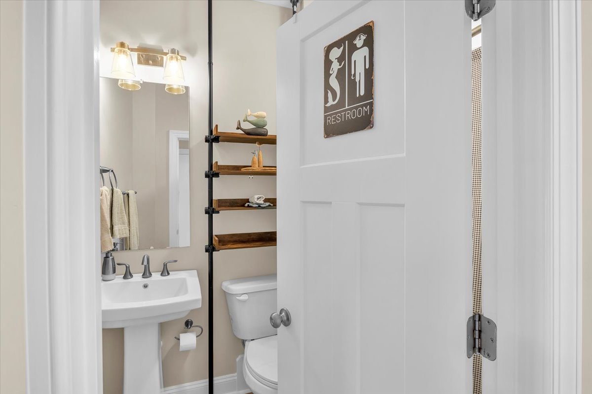 Your private bathroom features a pedestal sink, smart storage shelves, and charming restroom sign—everything you need for a comfortable stay.