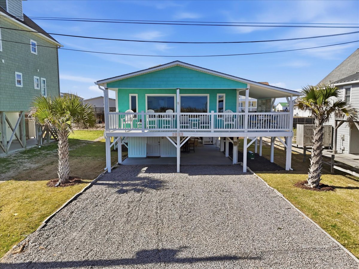 Charming coastal cottage elevated on stilts with convenient parking, wraparound deck, and tropical palms in a peaceful neighborhood setting.