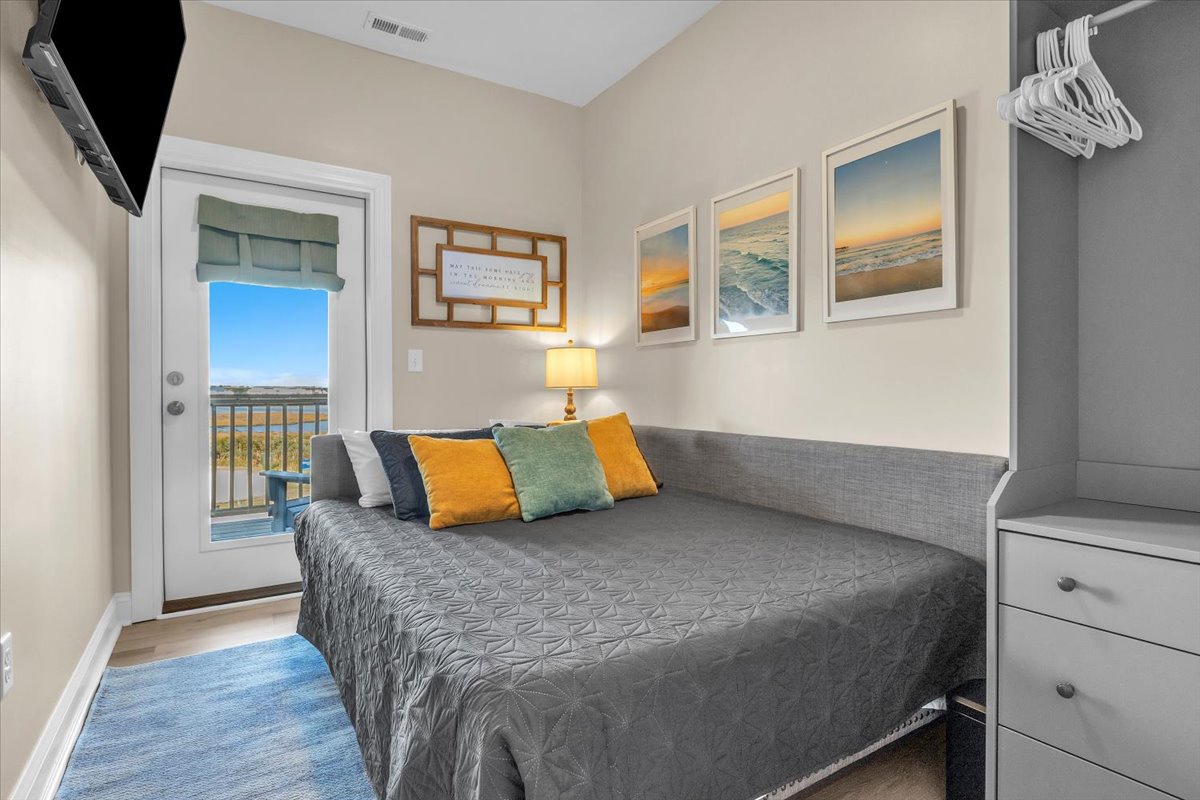 Rest peacefully in your cozy bedroom featuring ocean artwork, vibrant pillows, and private balcony access to waterfront views.