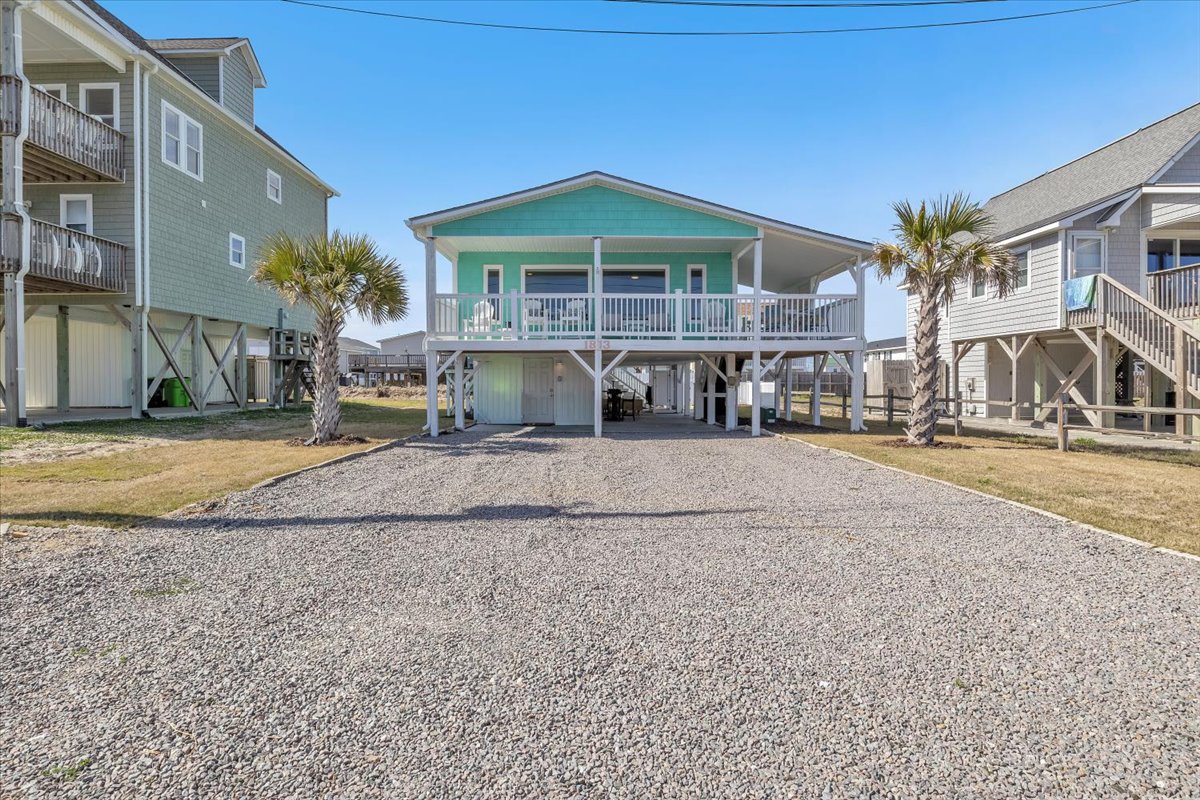 Coastal beach house elevated on stilts with spacious parking and charming turquoise exterior nestled among neighboring vacation homes.