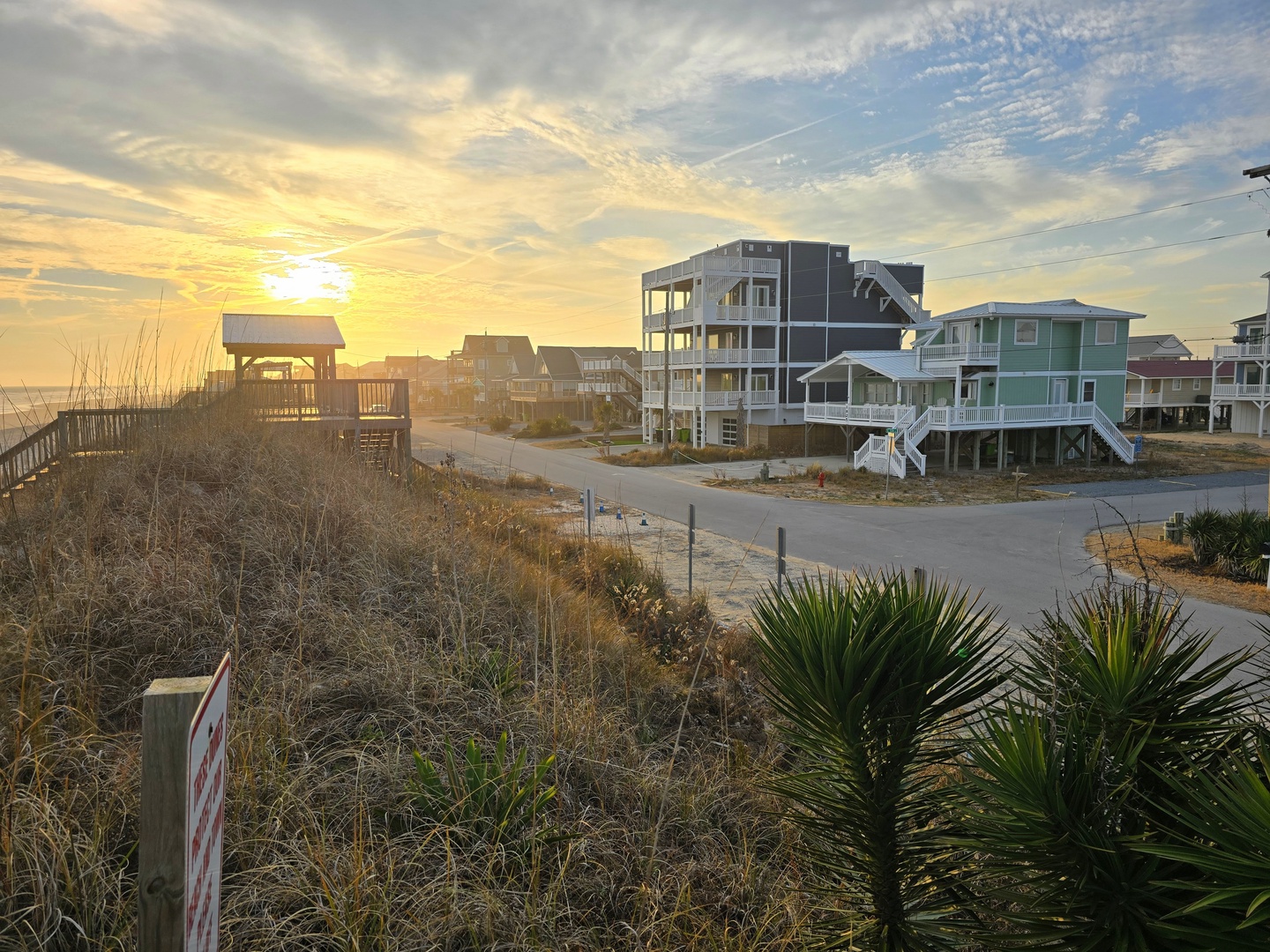 Stunning beachfront community showcasing colorful coastal homes and elevated properties along pristine sandy shores during golden hour.