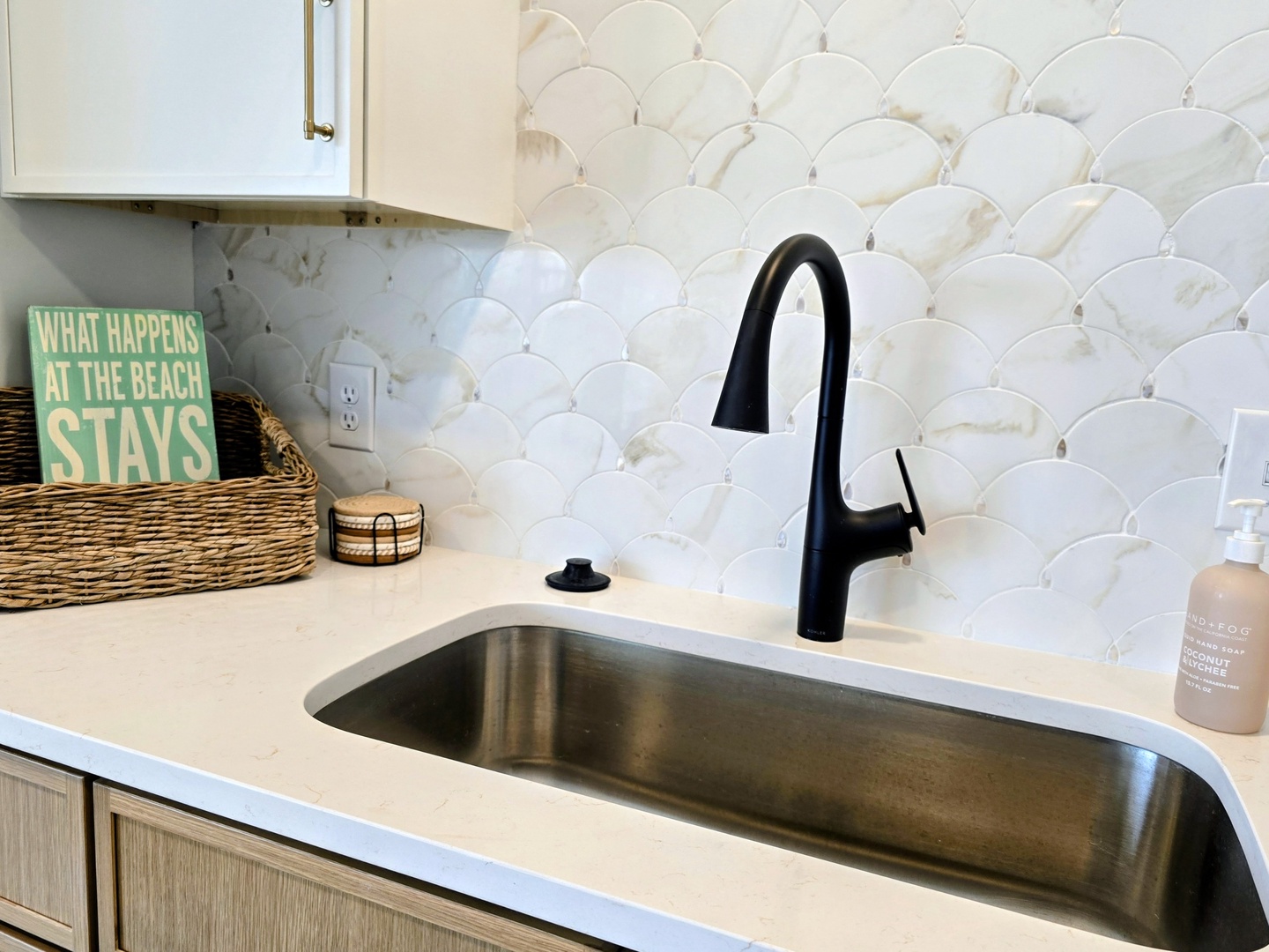 Your stylish kitchen features a deep sink with sleek black faucet, stunning scale-pattern backsplash, and charming coastal touches that make cooking feel like a vacation.