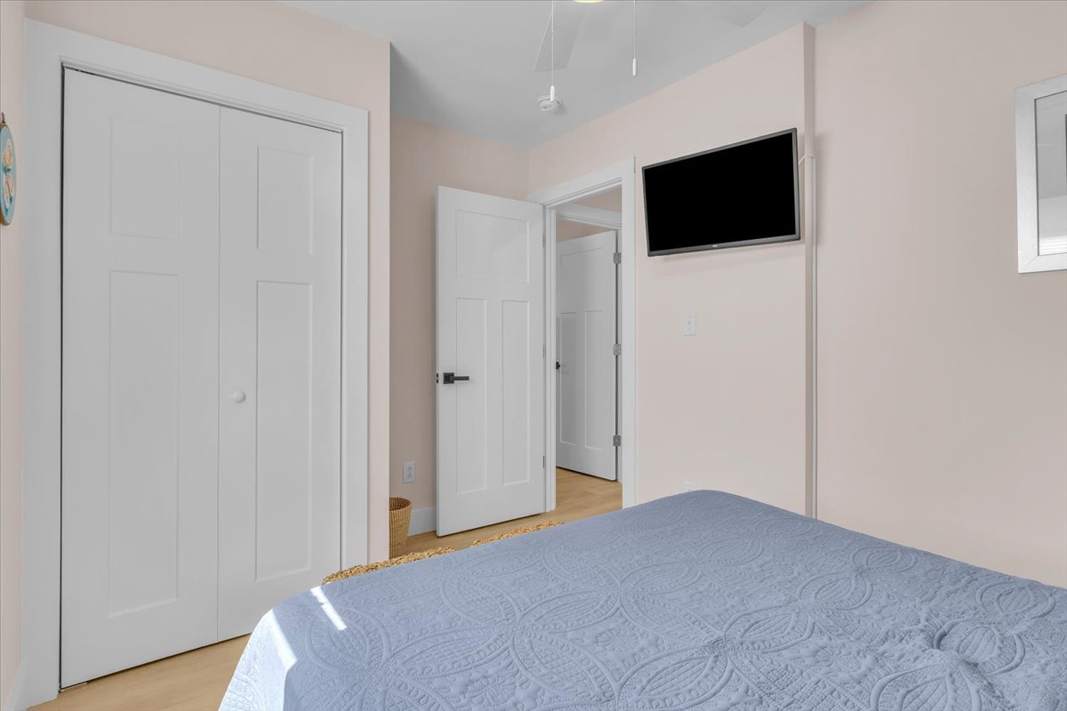 Your serene bedroom features a wall-mounted TV for relaxing evenings, with crisp white linens and ample storage in the built-in closet.