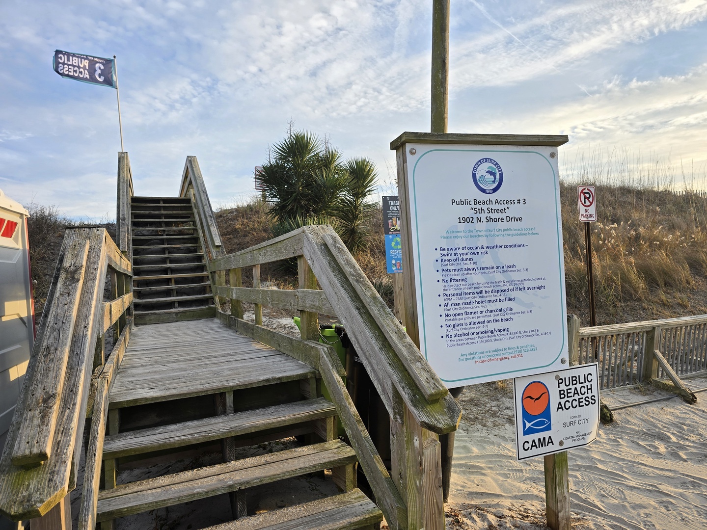 Public beach access with wooden boardwalk and informational signage leading to coastal area.