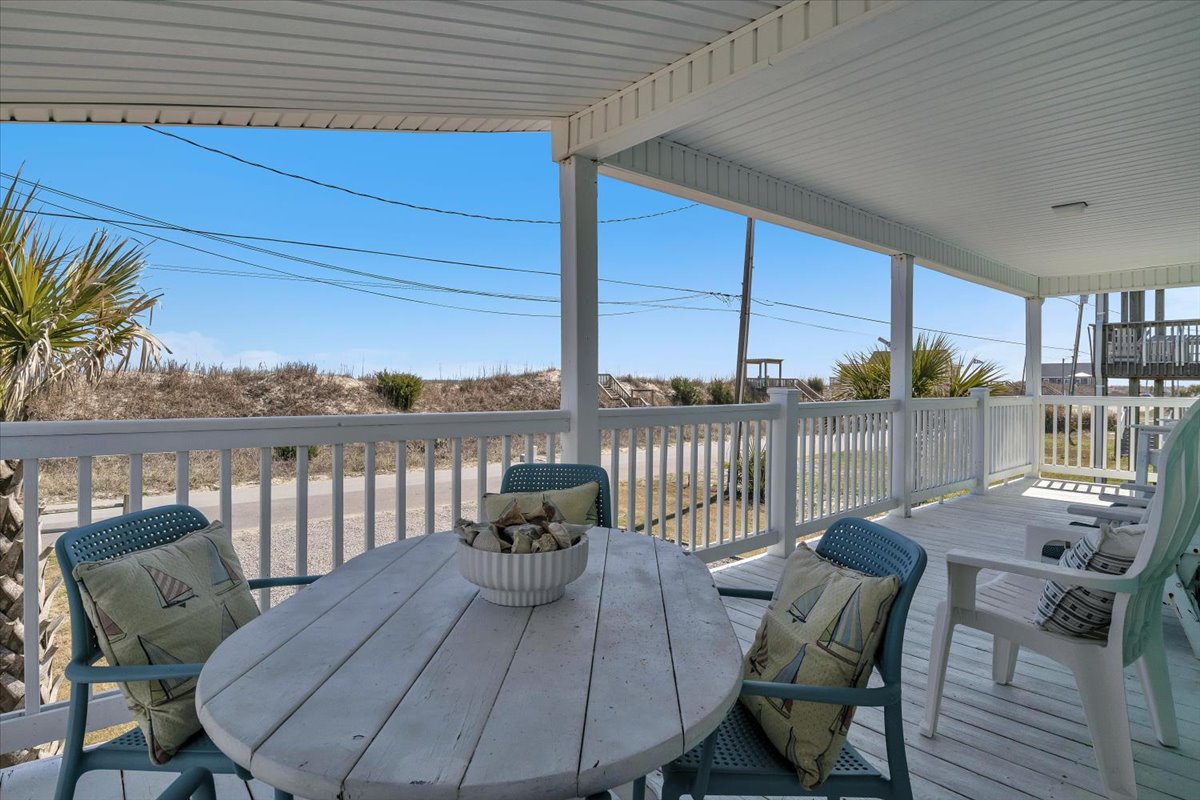 Your covered deck offers coastal dining with ocean breezes and stunning dune views through white railings.