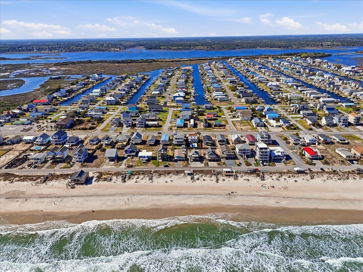 Stunning aerial view of beachfront community with colorful homes lining pristine sandy shores and calm bay waters beyond.