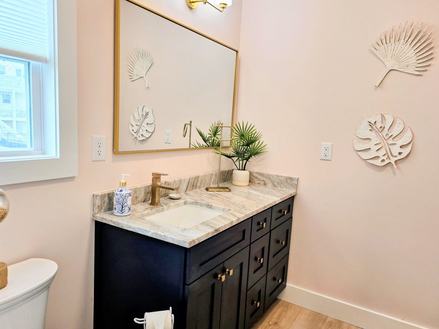 Refresh in your stylish bathroom with marble countertops, brass fixtures, and tropical leaf art creating a serene spa-like atmosphere.