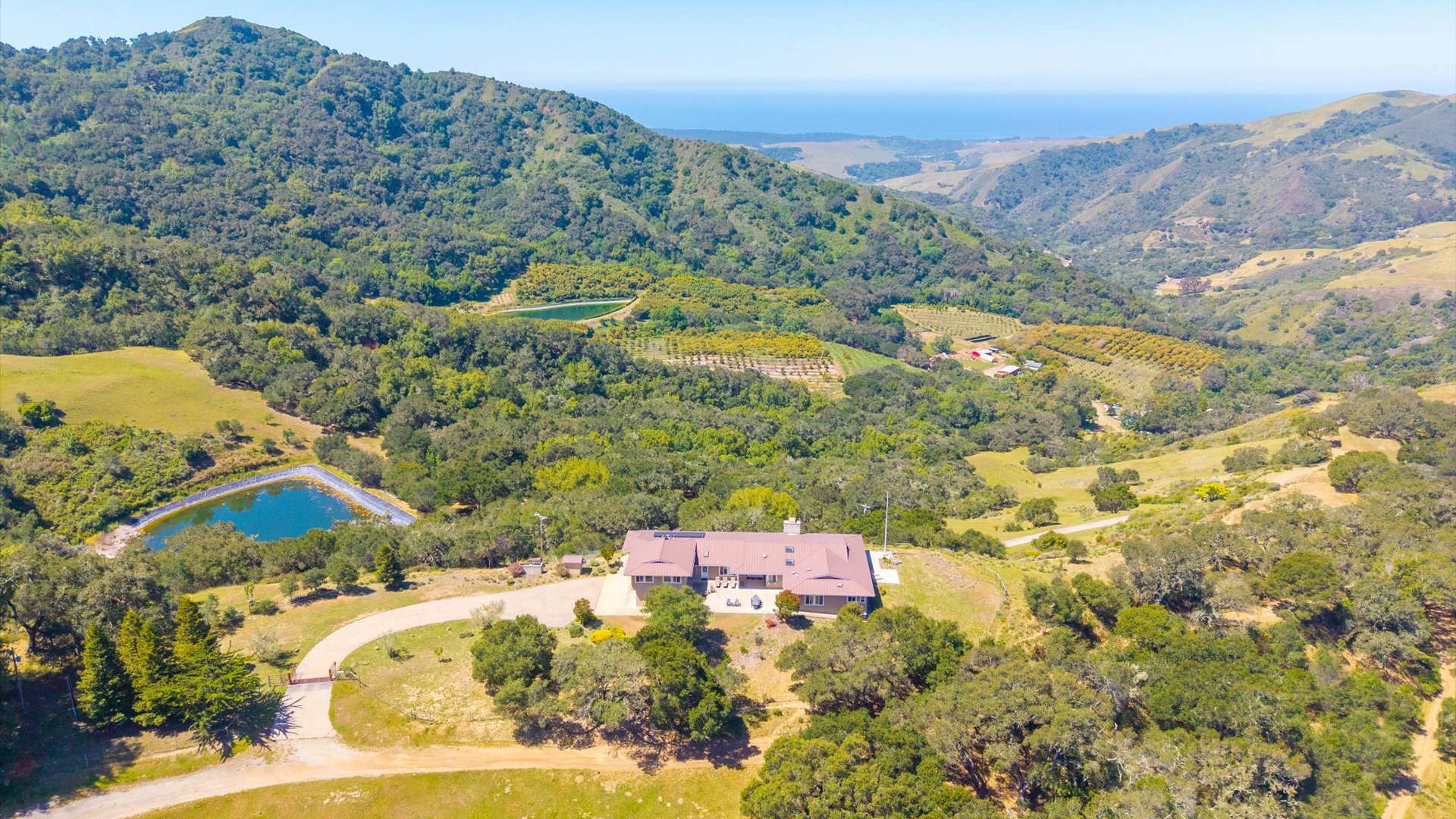 Aerial view of the property nestled among rolling hills, surrounded by orchards, with distant ocean and mountain views.