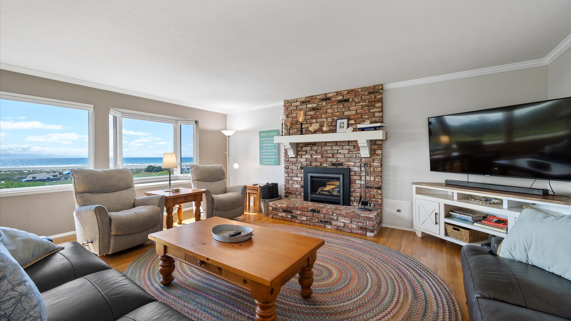 The living room has a flat screen TV and fireplace with wall to wall windows feauring ocean views