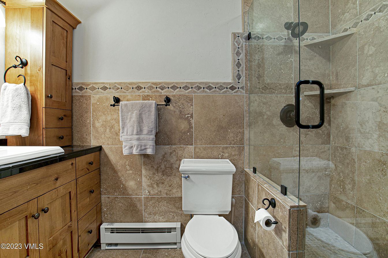 Step into your beautifully tiled bathroom where rustic wood cabinetry meets elegant stone tile. Enjoy your private glass-enclosed shower with built-in shelving after a day exploring.