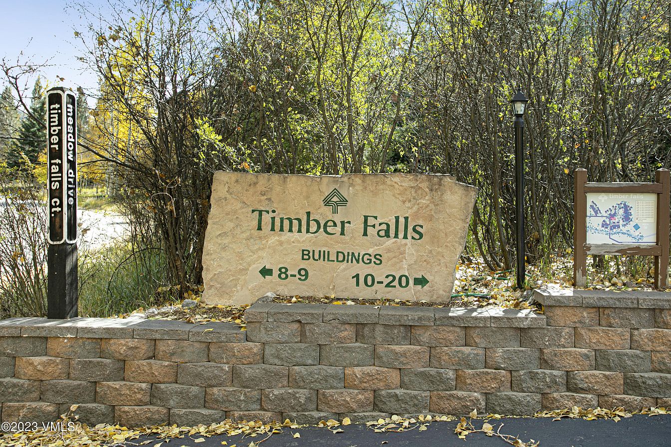 The Timber Falls property sign marks the entrance to this mountain community, surrounded by natural wooded landscape and autumn foliage.
