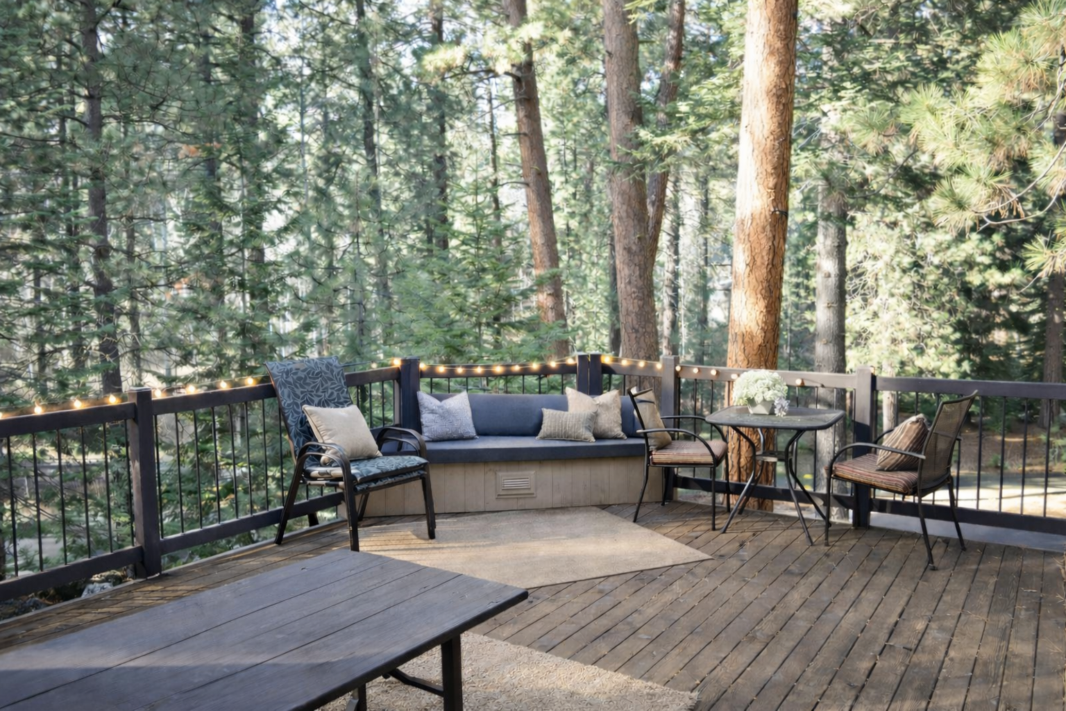 Unwind on your private deck surrounded by towering pines, where string lights and cozy seating create the perfect evening retreat.