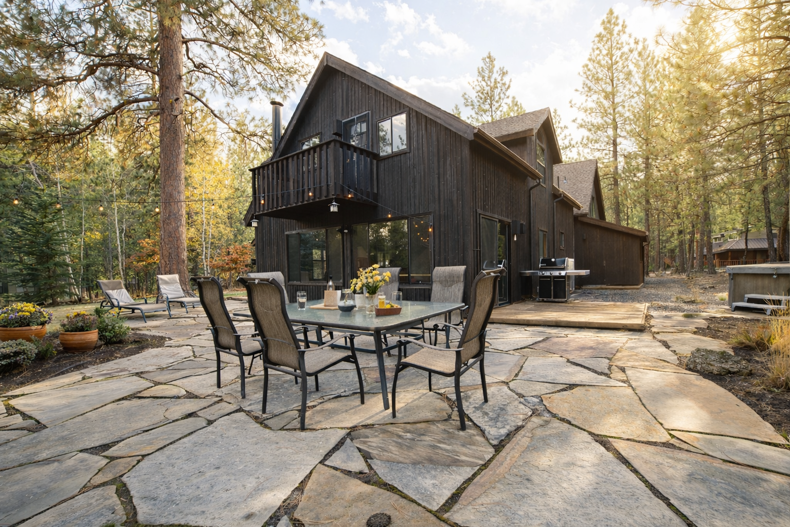 Modern cabin nestled among towering pines with spacious stone patio and mountain views.