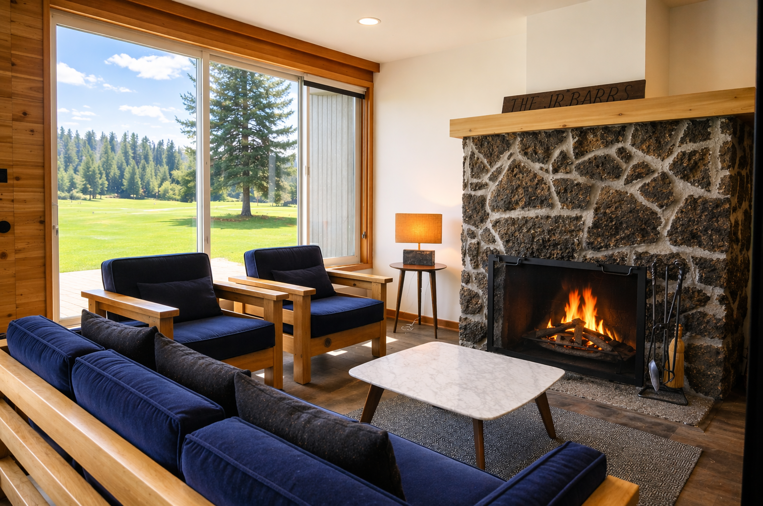 Cozy up by the crackling stone fireplace while gazing out at serene forest views through floor-to-ceiling windows in this warm, inviting living space.