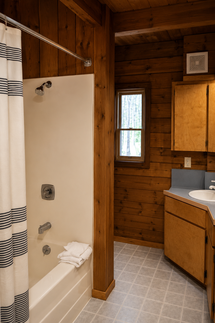 Step into your private bathroom, where rustic wood-paneled walls meet modern comforts, offering you a warm shower-tub combo and fresh towels waiting just for you.