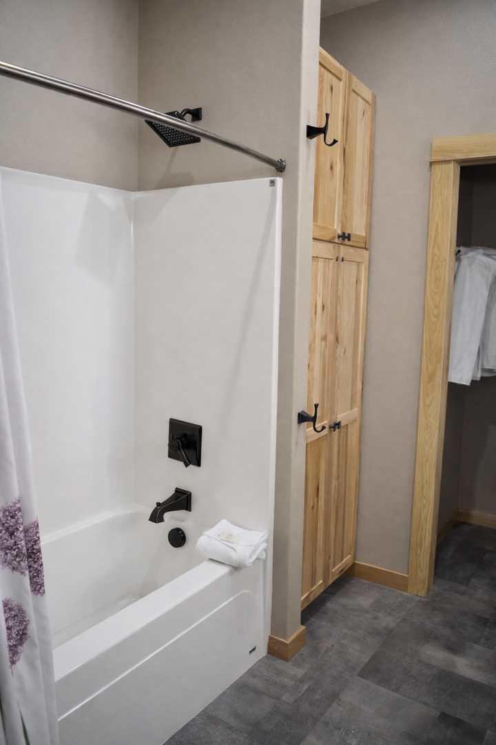 Unwind in your spacious bathroom featuring a deep soaking tub with overhead rainfall shower and warm wood cabinetry for all your essentials.