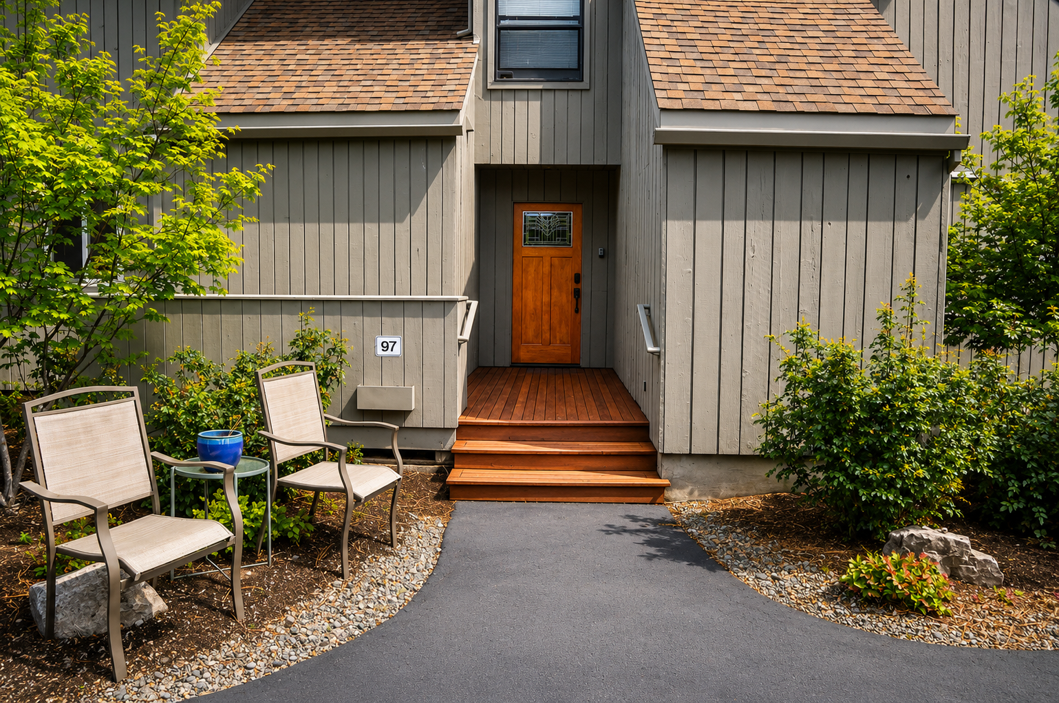 The property entrance features a warm wooden doorway framed by lush greenery and inviting outdoor seating, marking your arrival at this peaceful retreat.